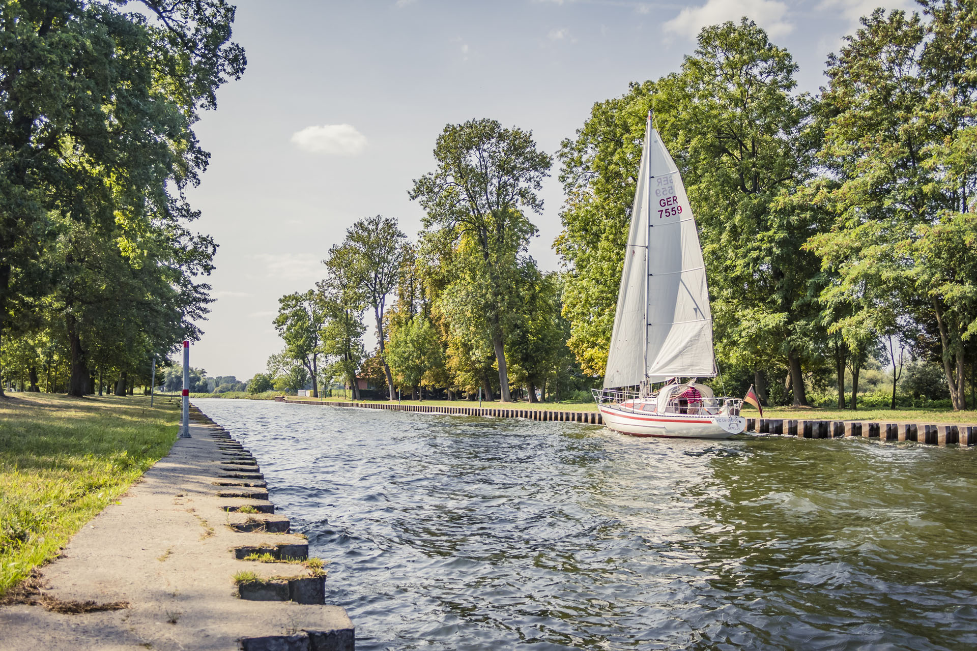 Entry towards the port of a sailboat. Trees and the bank edge are attached to the left and right.